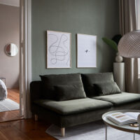 a living room with dark green walls and couch with two art prints on the wall with the title; The Pen 02 and The Dot