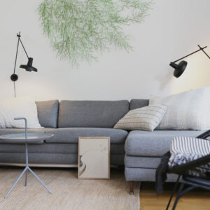 The Branch 01 art print in a thin oak frame standing on the floor in front of a grey sofa